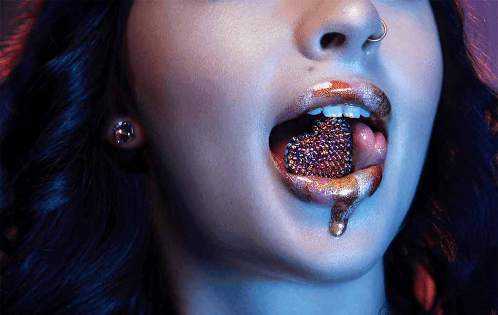 A swarovski crystal heart resting in the mouth of a model dripping with glitter.